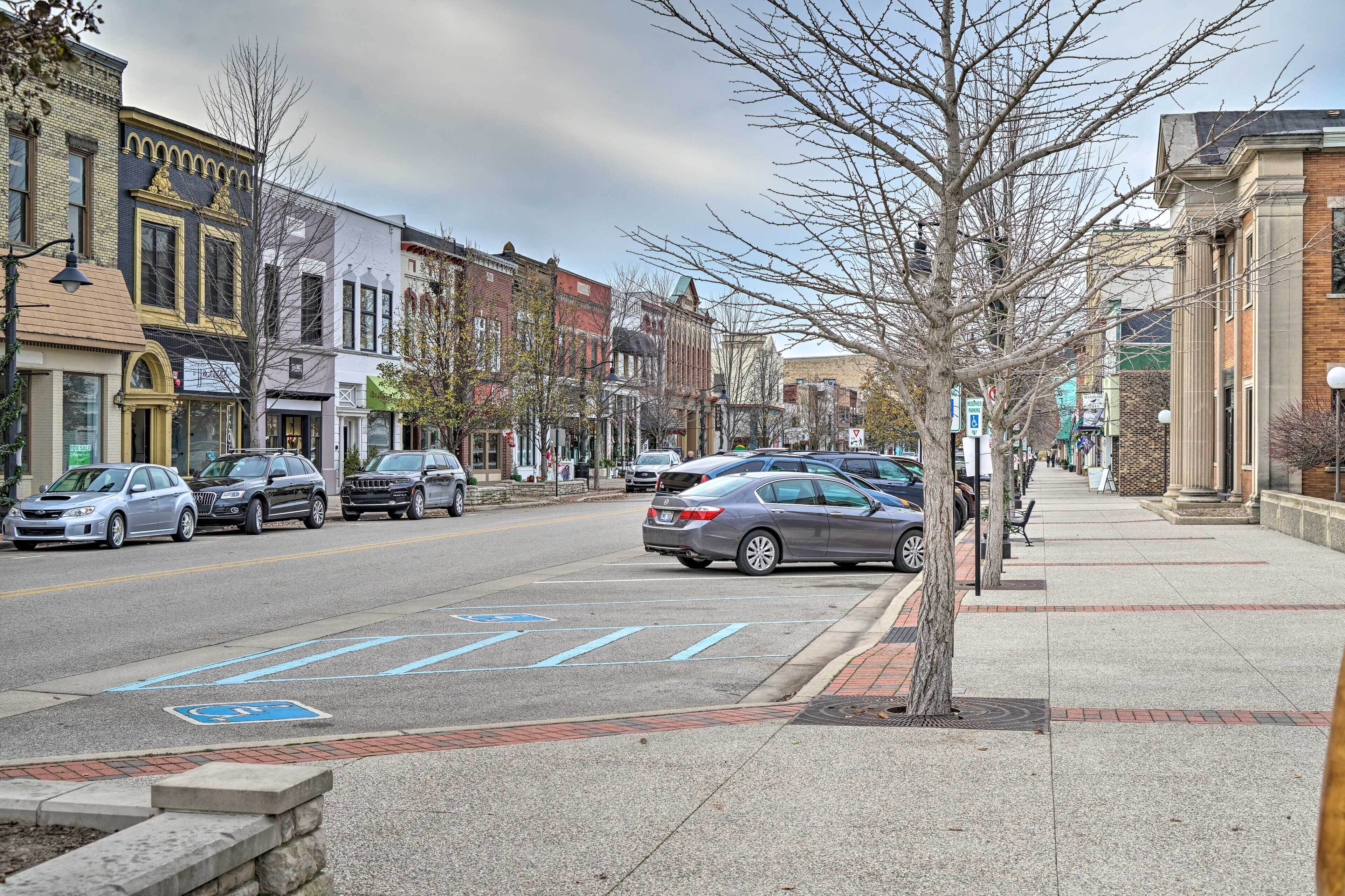 A street with parked cars, a sidewalk, and buildings with commercial establishments.