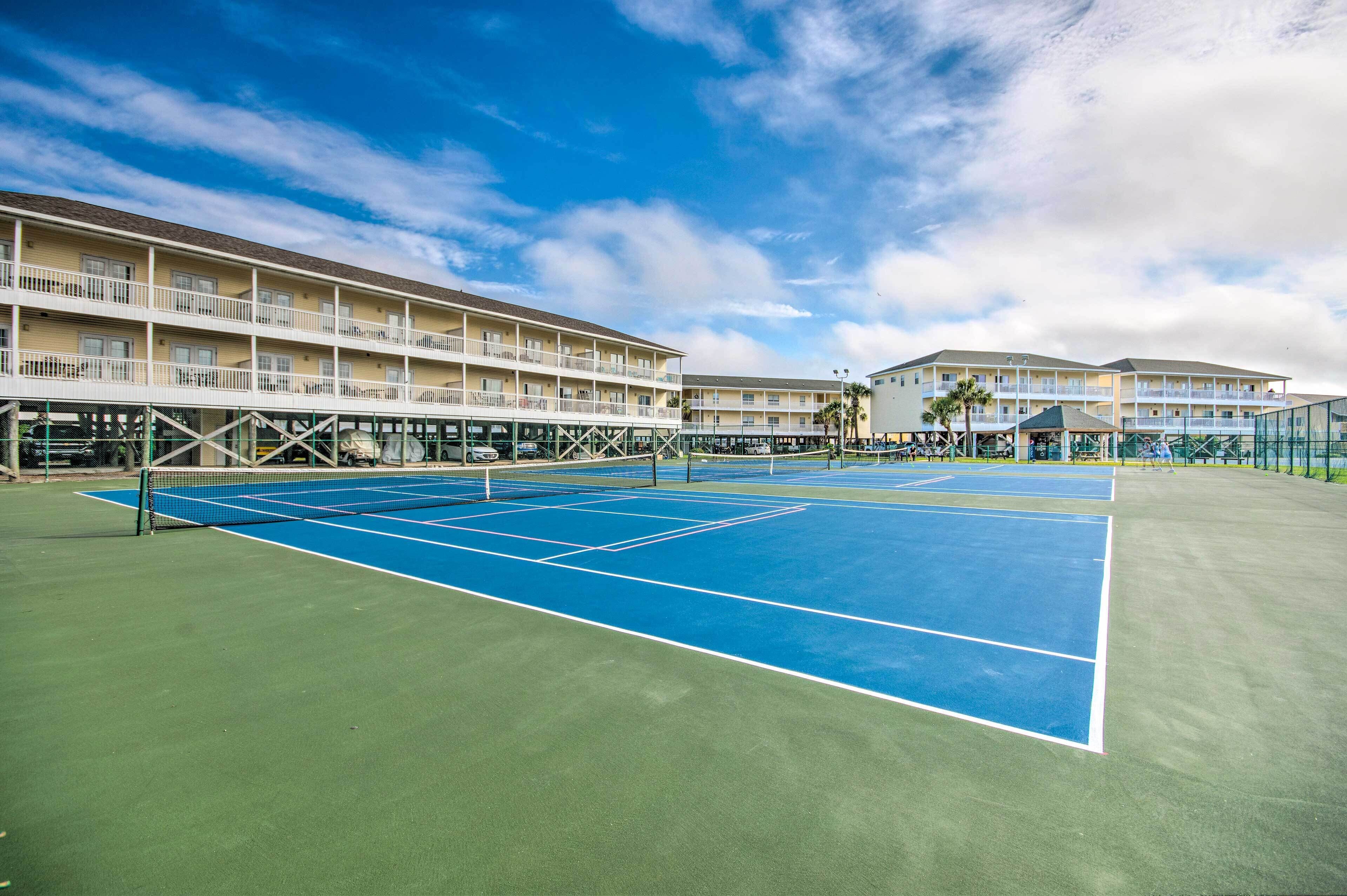A tennis court with a net, surrounded by a multi-story building with balconies.