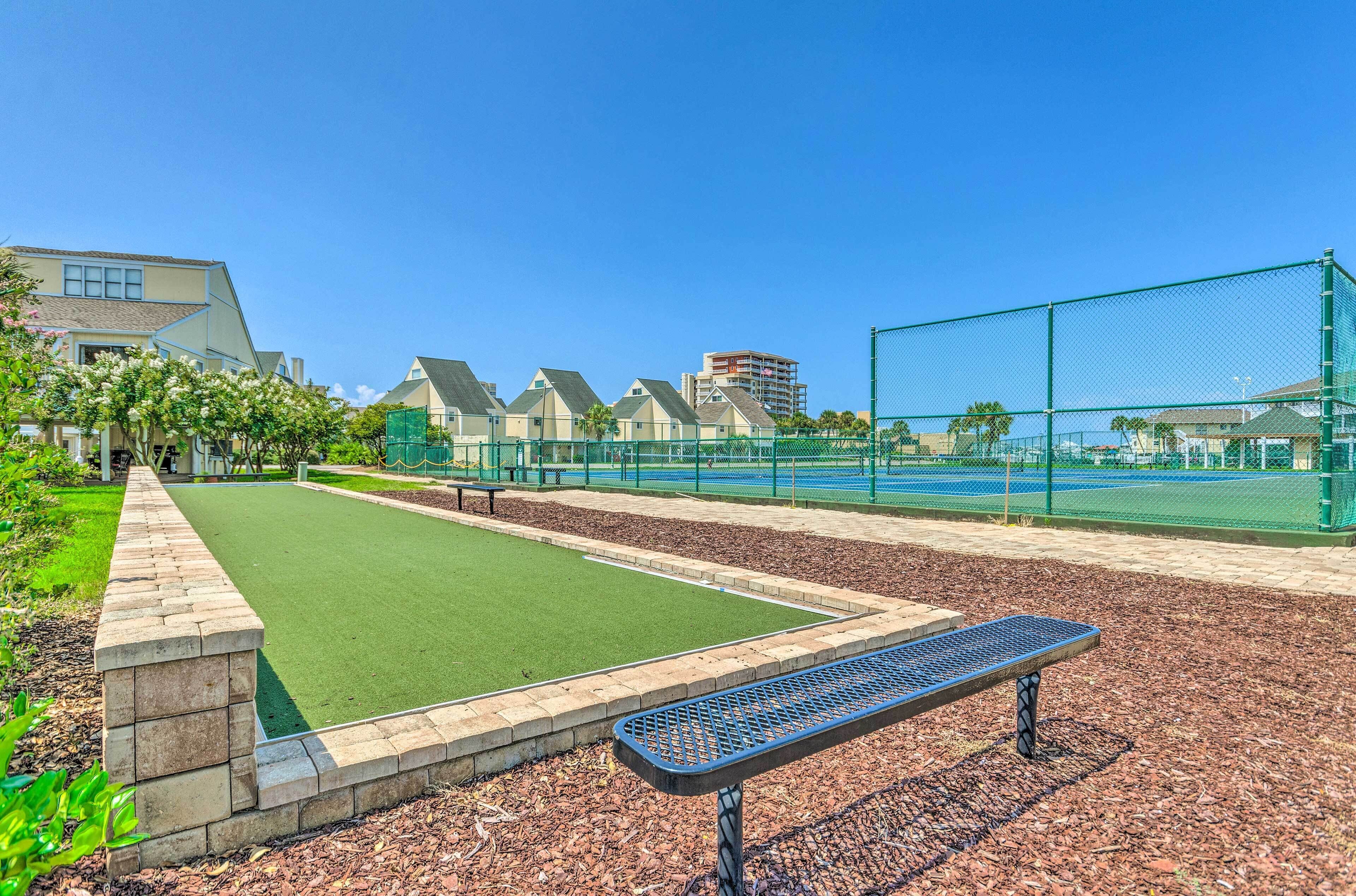 A tennis court with a green fence, a bench, and a brick wall.