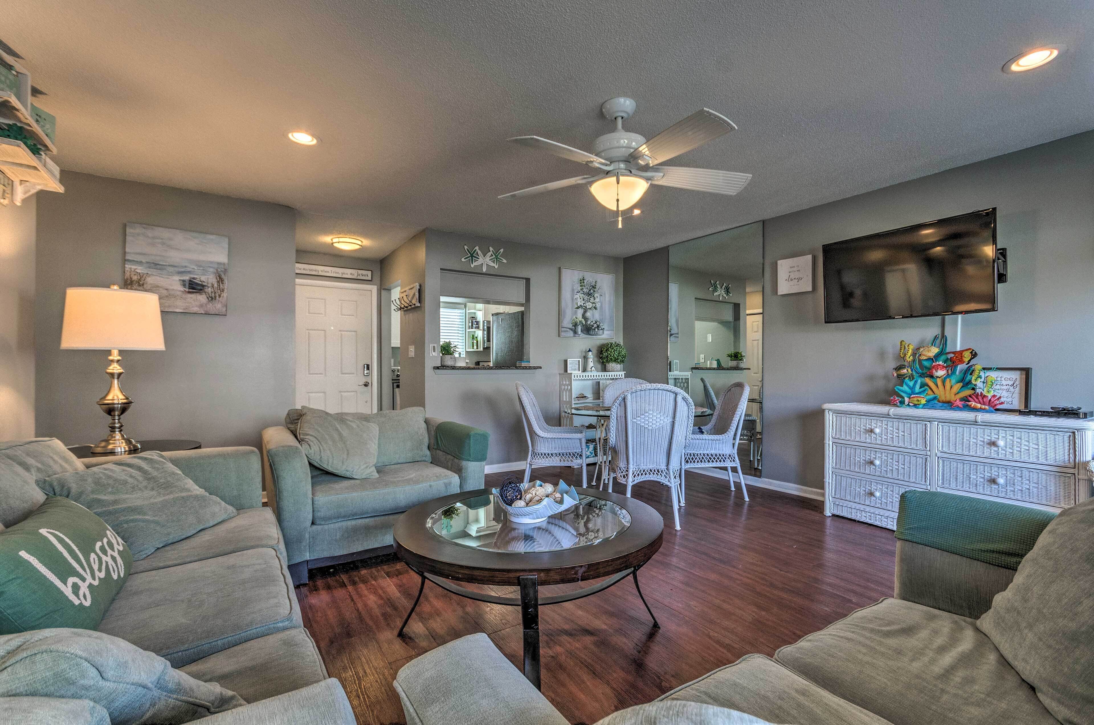 A living room with a ceiling fan, a television mounted on the wall, and a dining area with wicker chairs.