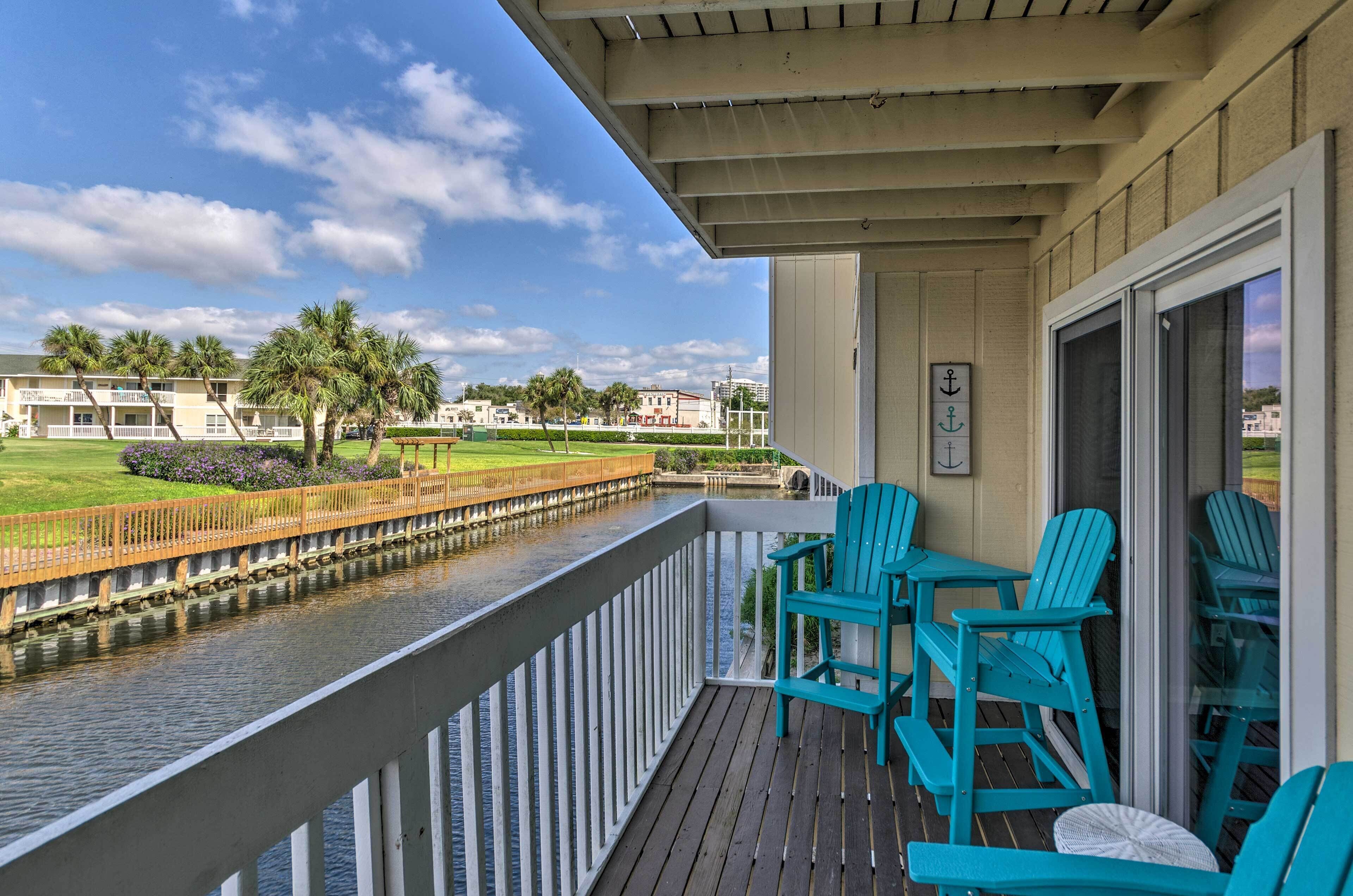 A balcony with turquoise Adirondack chairs and a view of a canal and buildings.
