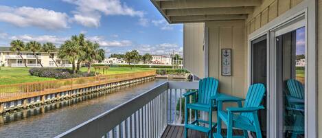 A balcony with turquoise Adirondack chairs and a view of a canal and buildings.
