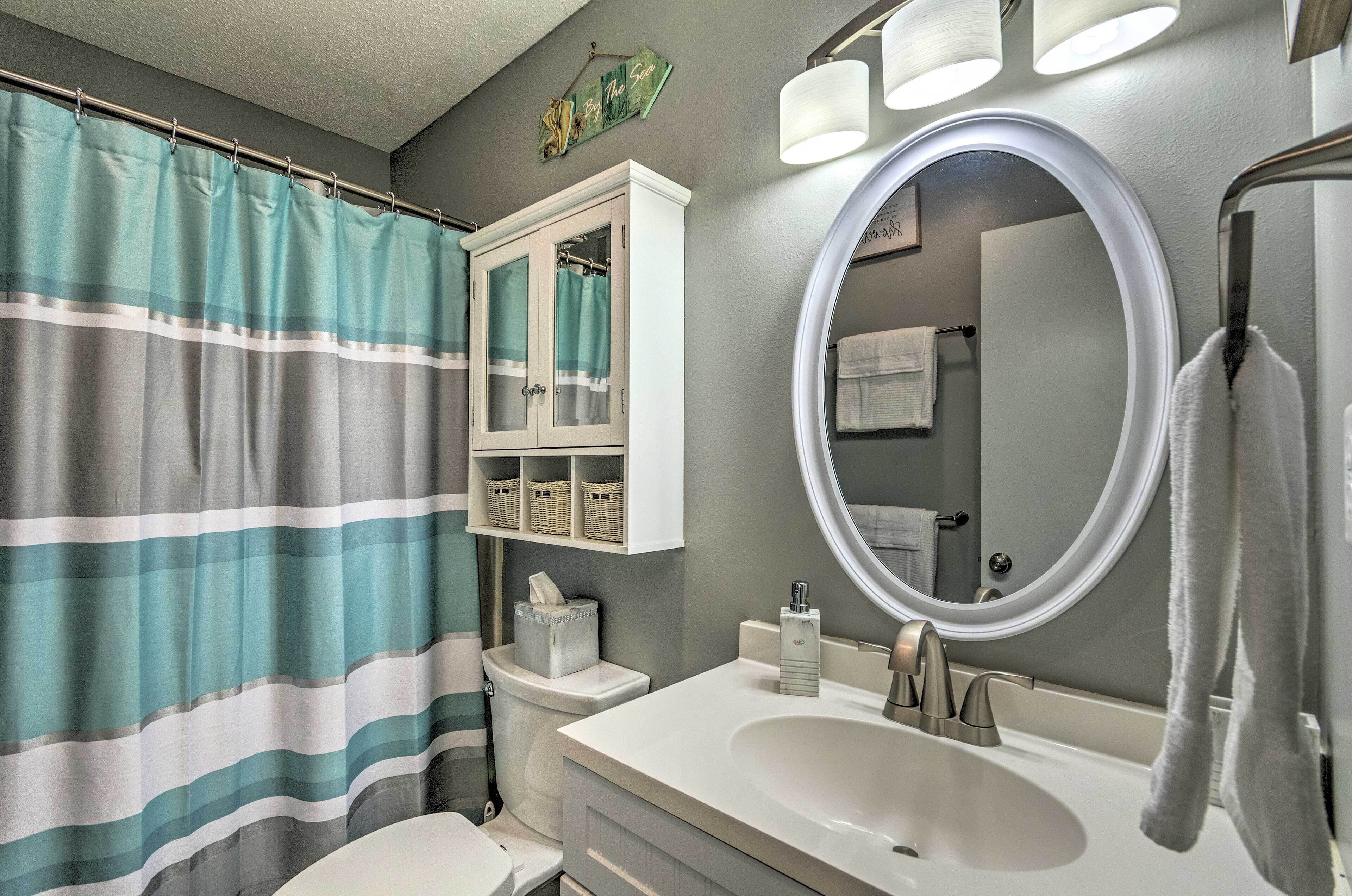 A bathroom with a striped shower curtain, a white vanity with a large mirror, and a toilet with a basket of toiletries.