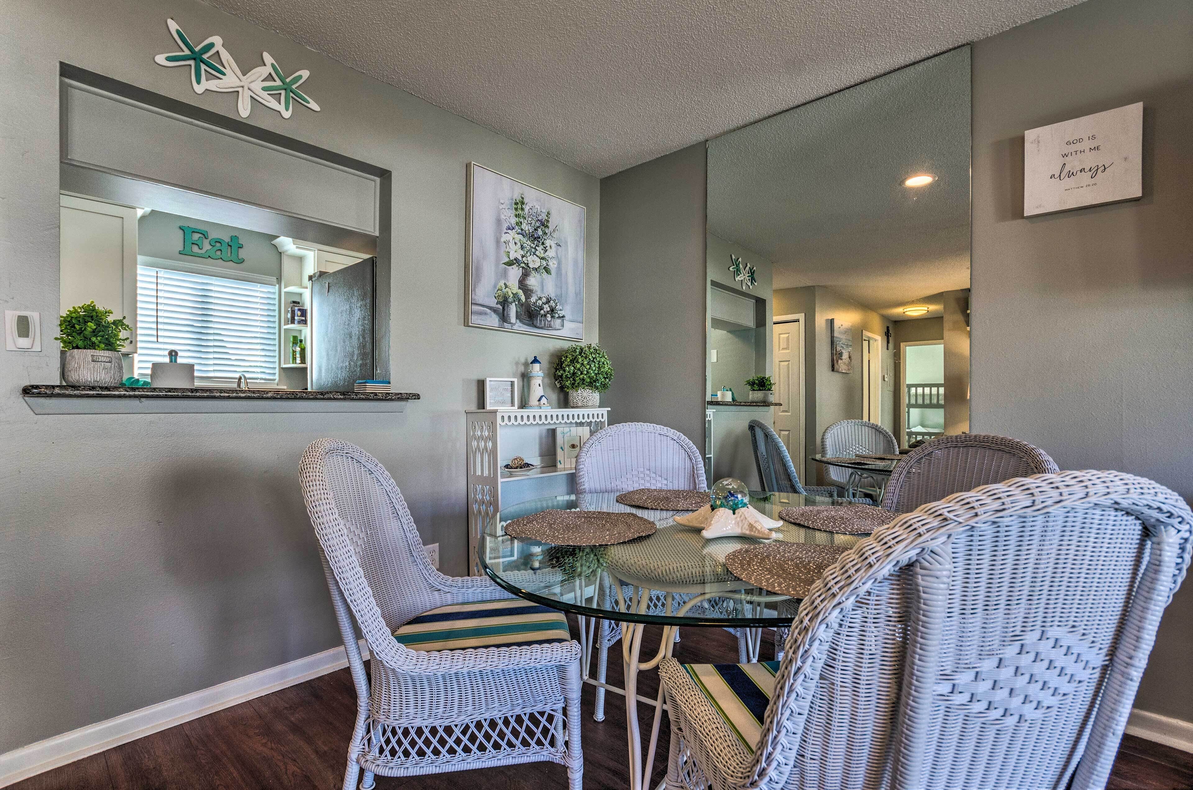 A dining area with wicker chairs, a glass table, and a mirror reflecting the room.
