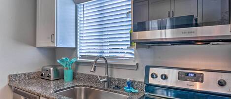 Una cocina moderna con lavavajillas de acero inoxidable, estufa Whirlpool y ventana con persianas.