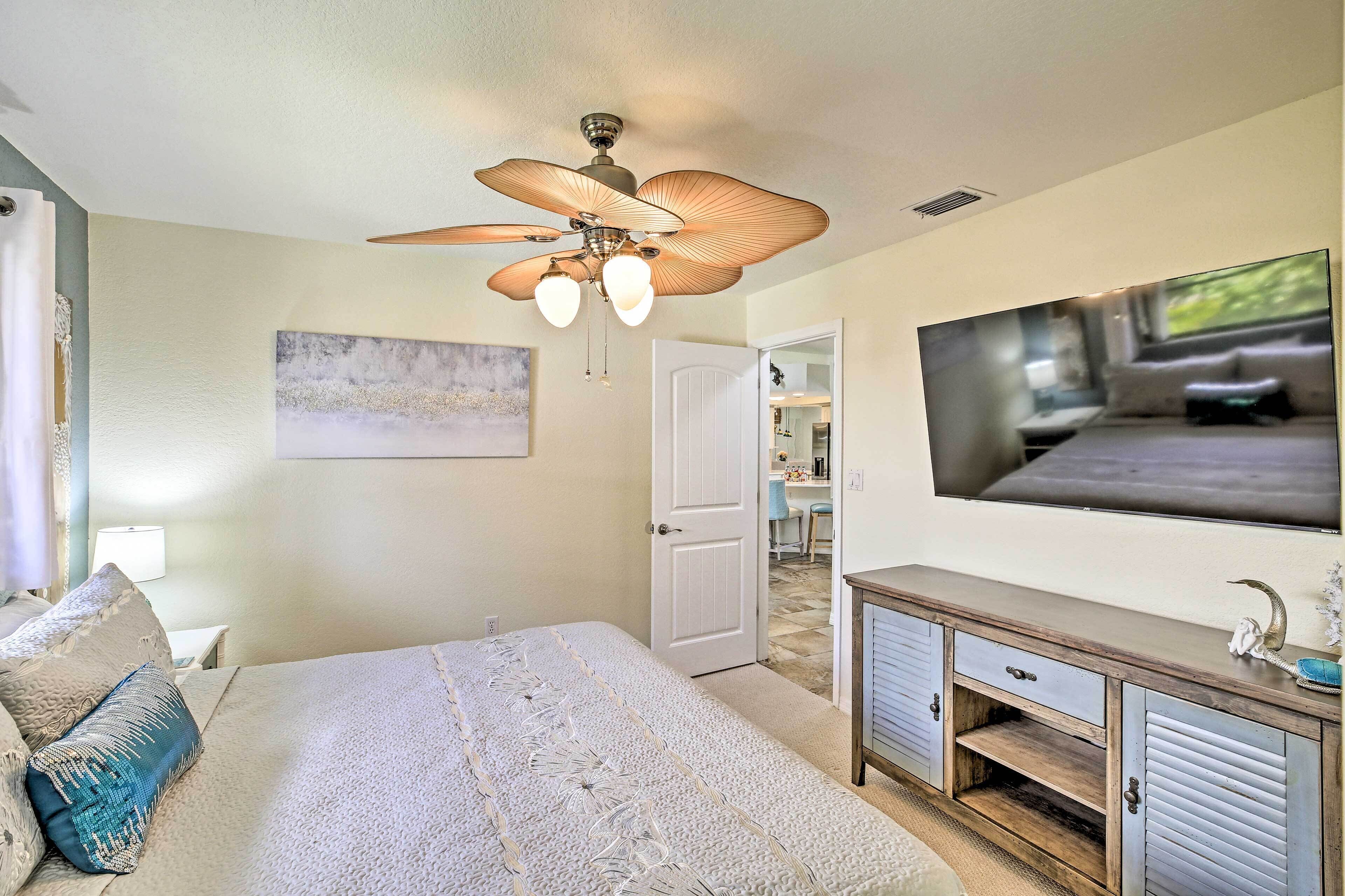 Quarto com cama, ventilador de teto, televisão e porta para um banheiro.