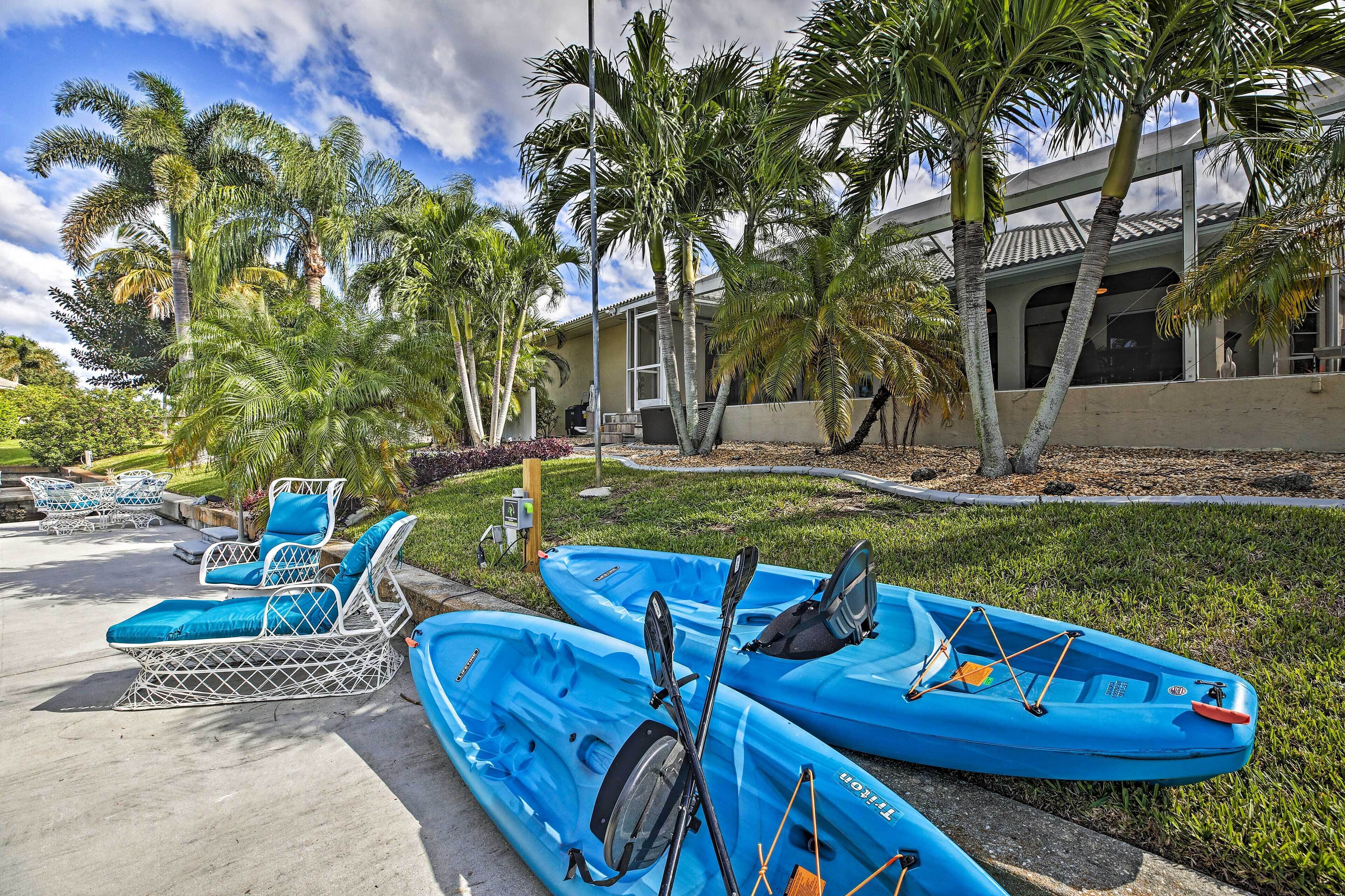 A pool area with lounge chairs and kayaks, surrounded by palm trees and a building with a tiled roof.