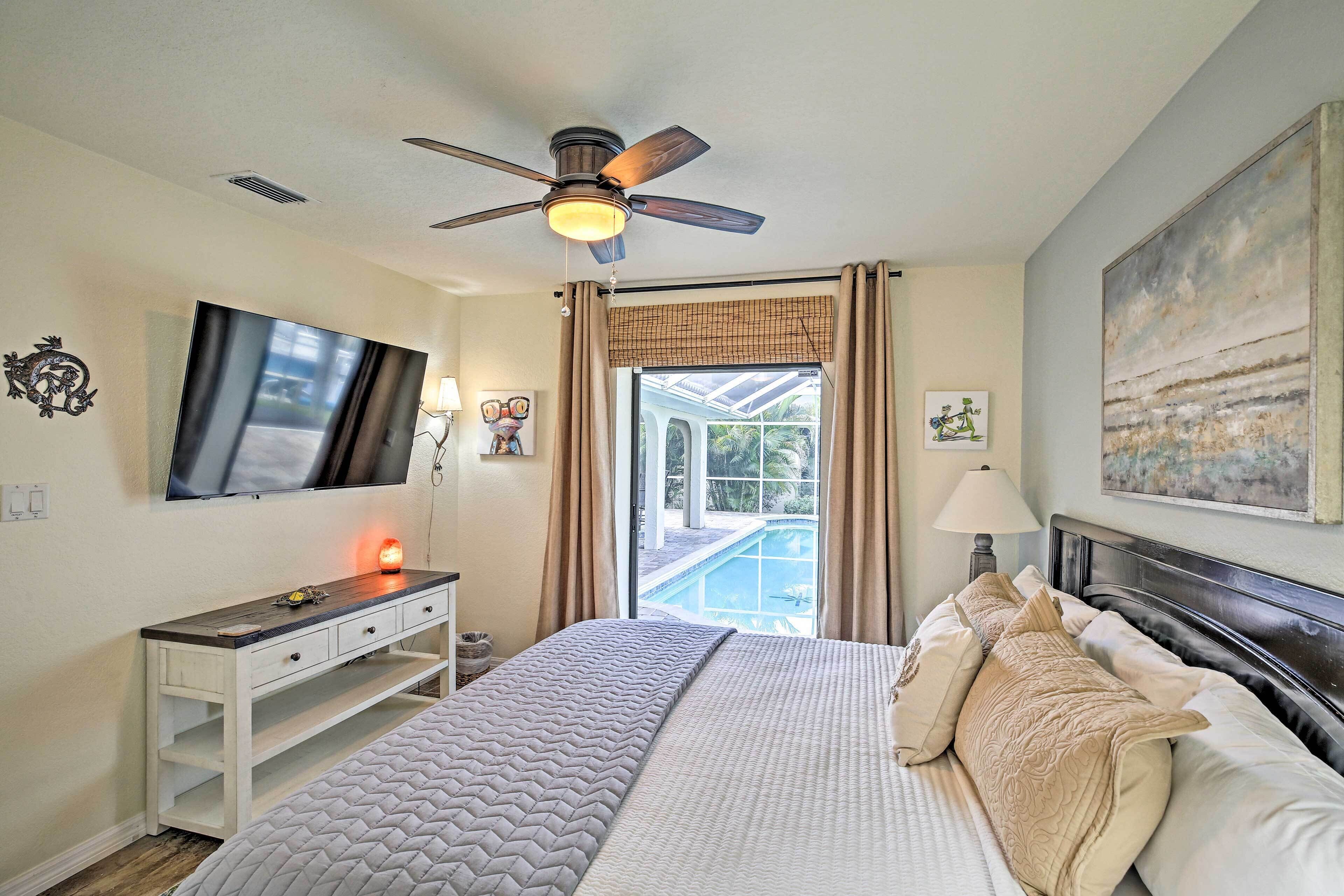 A bedroom with a bed, a desk, a television, a ceiling fan, and a view of a swimming pool.