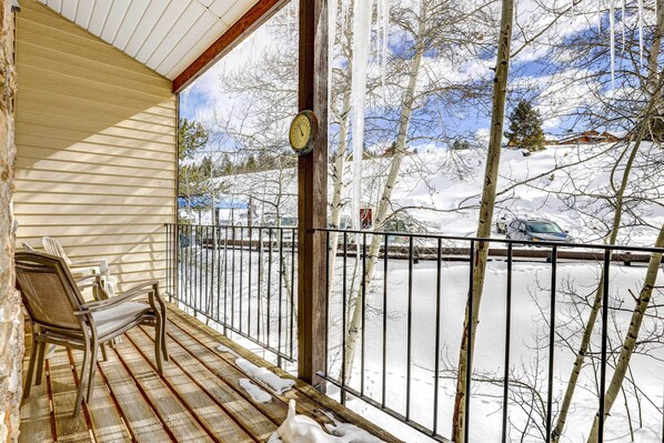 A wooden deck with chairs, a clock, and a view of a snowy landscape with bare trees and a car on a road.