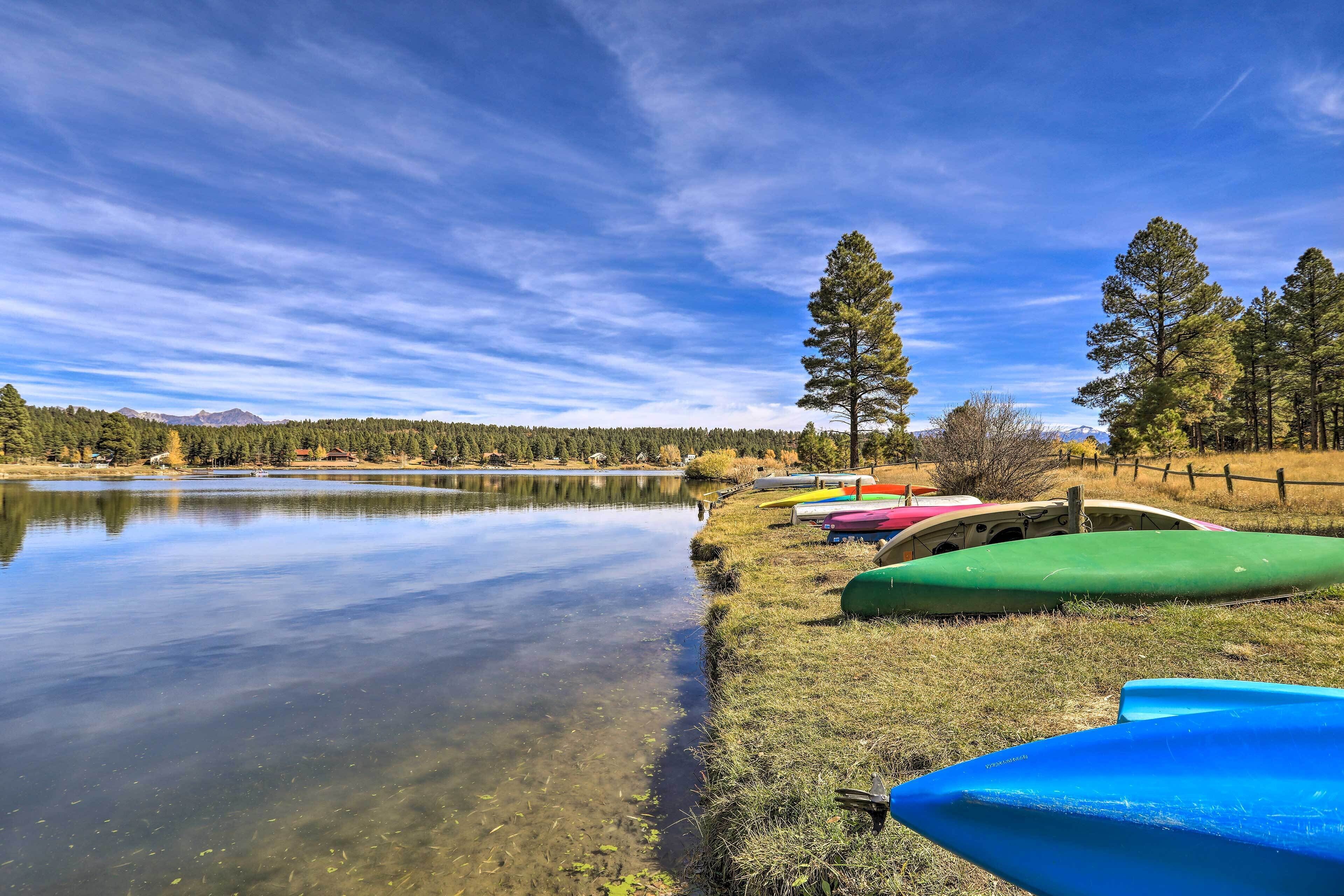 A calm lake with clear water, surrounded by a grassy area with several colorful kayaks and a wooden fence.