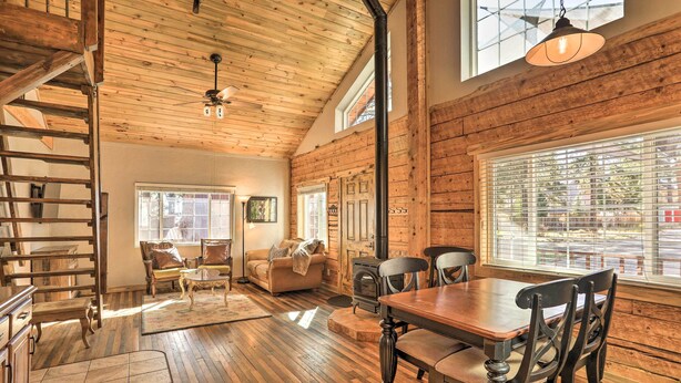 A spacious living area with a wooden ceiling, a fireplace, a dining table with chairs, and a staircase. - Tasteful Log Cabin Retreat on Lake Pagosa! (Pagosa Springs)