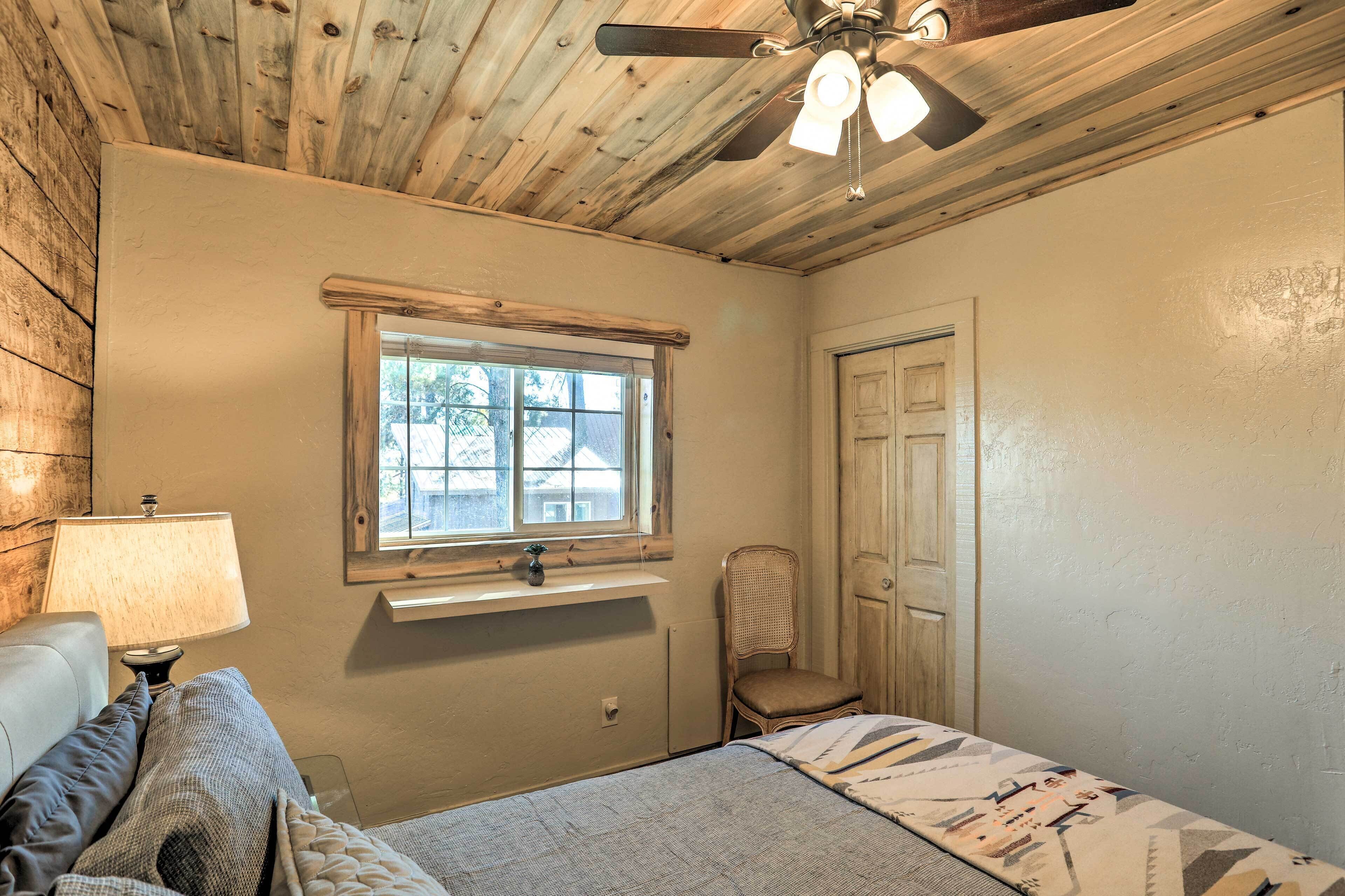 Un dormitorio con techo de madera, una ventana con vistas, una silla, una cama y una mesita de noche con lámpara.