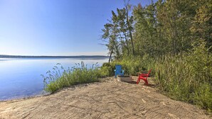 A sandy beach with a clear view of a calm lake and distant land. - Interlochen Home on Green Lake w/ Dock & Beach! (Interlochen)