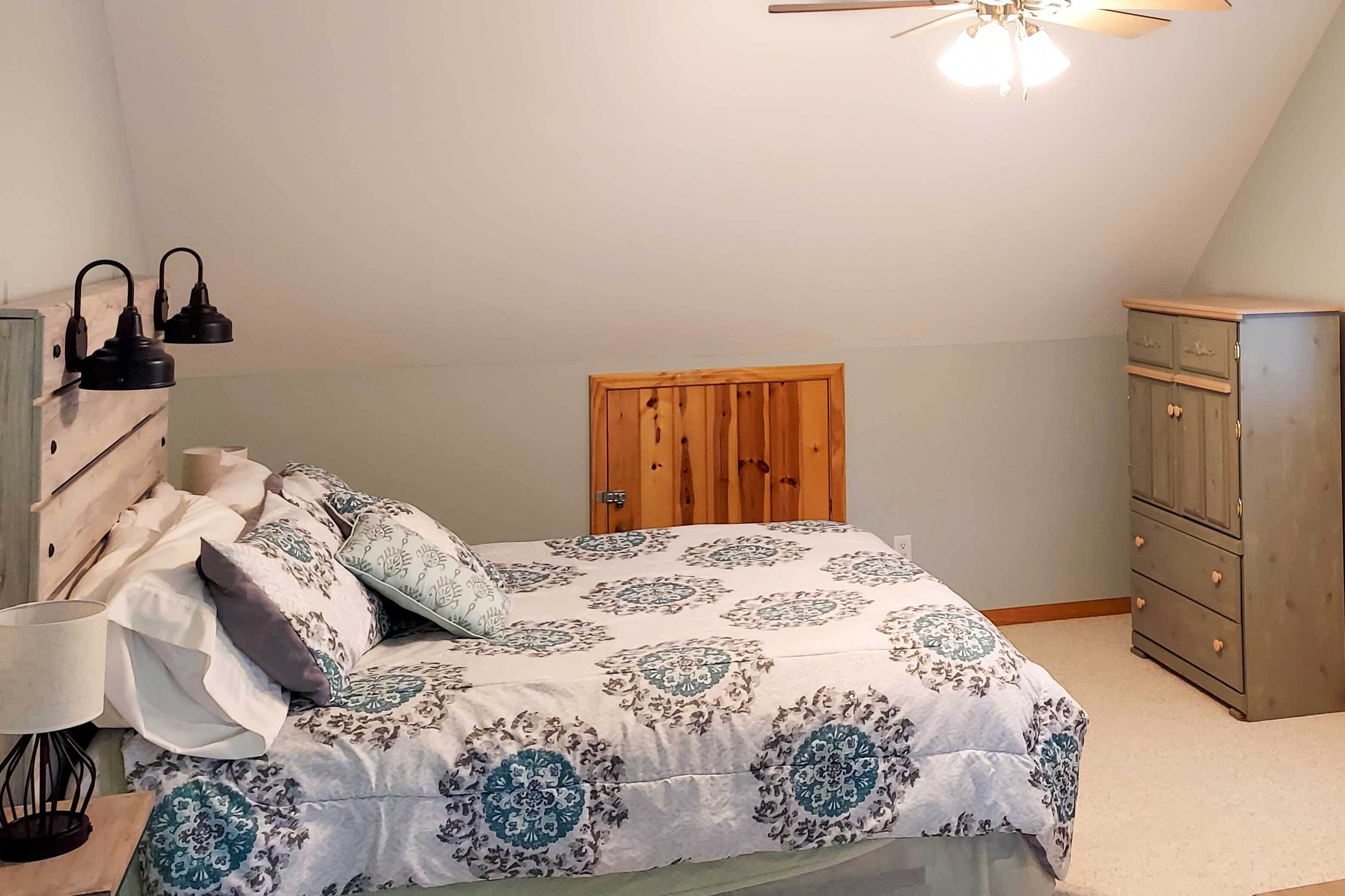 A bedroom with a bed, a wooden wardrobe, a ceiling fan, and two wall-mounted lamps.