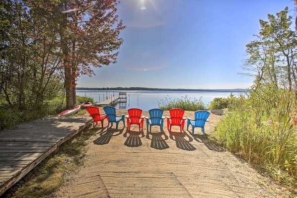 A wooden dock leading to a row of Adirondack chairs facing a lake. - Interlochen Home on Green Lake w/ Dock & Beach! (Interlochen)