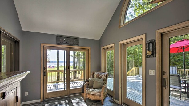 A room with a wicker chair, a wooden deck, and a view of the outdoors. - Interlochen Home on Green Lake w/ Dock & Beach! (Interlochen)