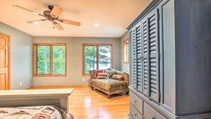 A bedroom with a bed, a dresser, a ceiling fan, and two windows with a view of trees. - Interlochen Home on Green Lake w/ Dock & Beach! (Interlochen)