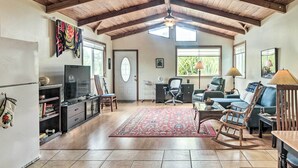 A spacious living area with a high ceiling, wooden beams, a television, a desk, a comfortable sofa, and a rocking chair. - P'hoa Home 4 Mi to Kilauea Caverns of Fire! (Pahoa)