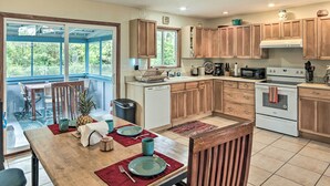 A modern kitchen with wooden cabinets, a dining area with a table set for four, and a view of the outdoors through large sliding glass doors. - P'hoa Home 4 Mi to Kilauea Caverns of Fire! (Pahoa)