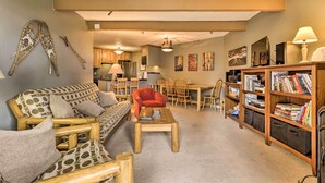 A cozy living room with a sofa, coffee table, and bookshelf. A dining area with chairs and a table is visible in the background. - Silverthorne Condo w/ Lake Views: 10 Mi to Skiing! (Silverthorne)