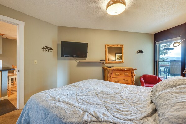 A bedroom with a bed, a dresser, a TV mounted on the wall, and a window with a view.