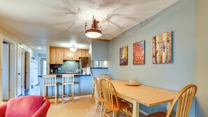A dining area with a wooden table and chairs, a red armchair, and a kitchen in the background. - Silverthorne Condo w/ Lake Views: 10 Mi to Skiing! (Silverthorne)