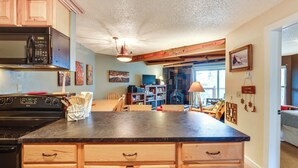 A kitchen with wooden cabinets, a black stove, and a black microwave. There is a dining area with a table and chairs, and a bookshelf filled with books. - Silverthorne Condo w/ Lake Views: 10 Mi to Skiing! (Silverthorne)