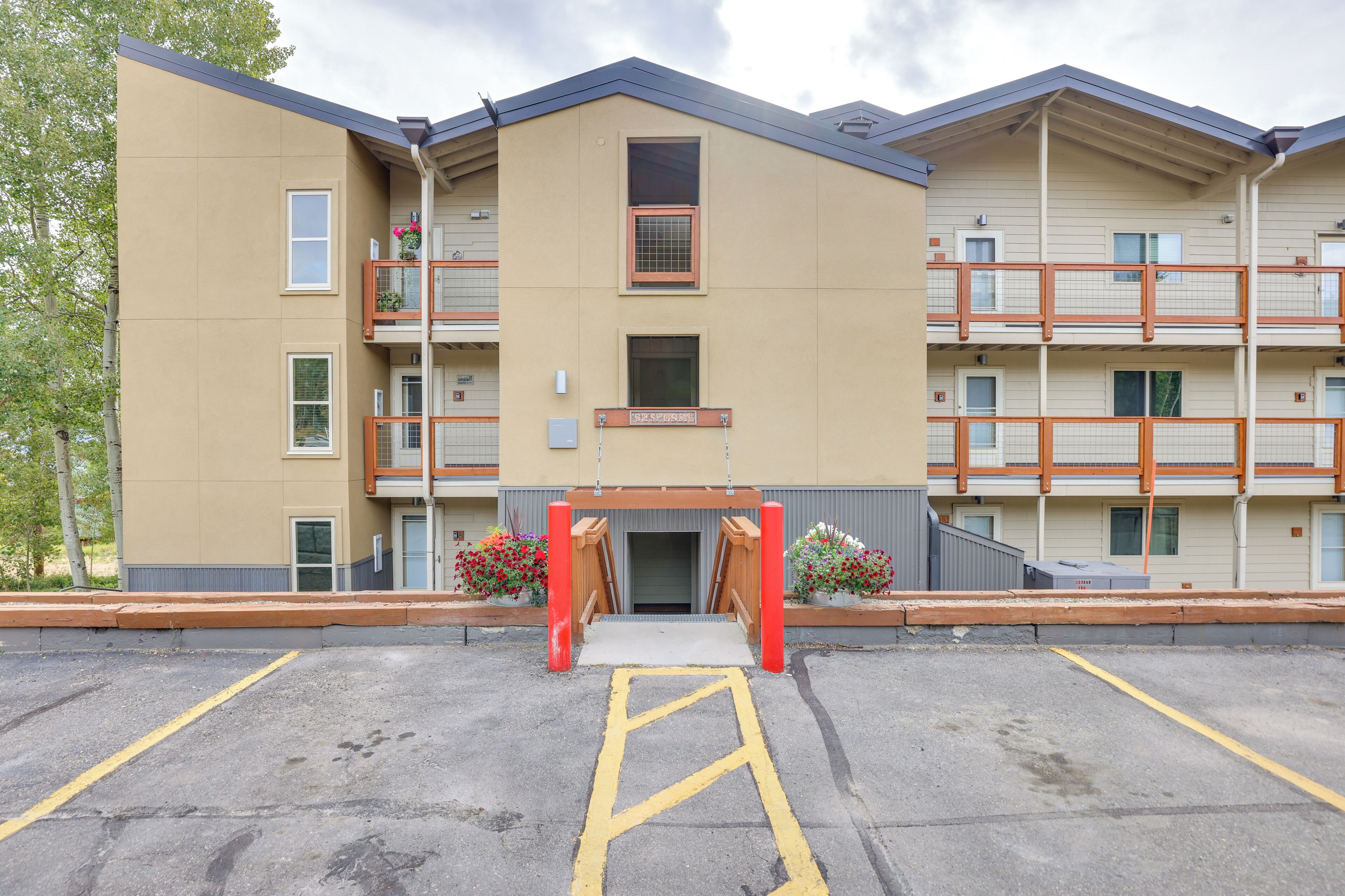 A multi-story building with a central entrance, balconies, and a parking area.