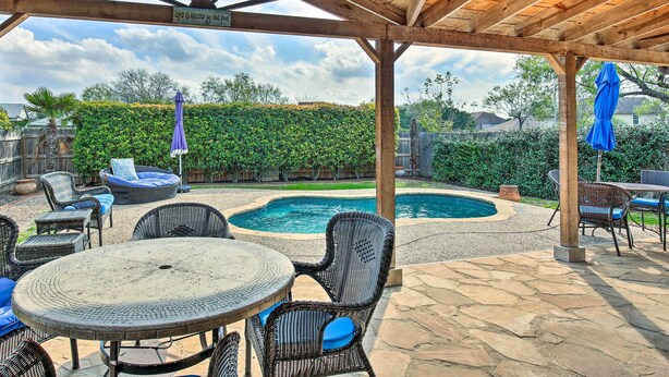 A covered outdoor patio with a pool, wicker furniture, and a stone floor.