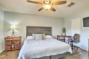 A bedroom with a bed, a nightstand with baskets, a desk with a chair, a ceiling fan, and a door. - San Antonio Getaway ~ 18 Mi to Dtwn + Pool! (San Antonio)