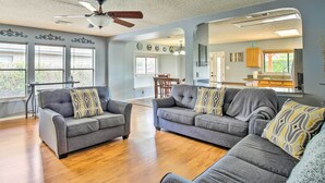 A spacious living room with two grey sofas, wooden flooring, a ceiling fan, and a dining area in the background.