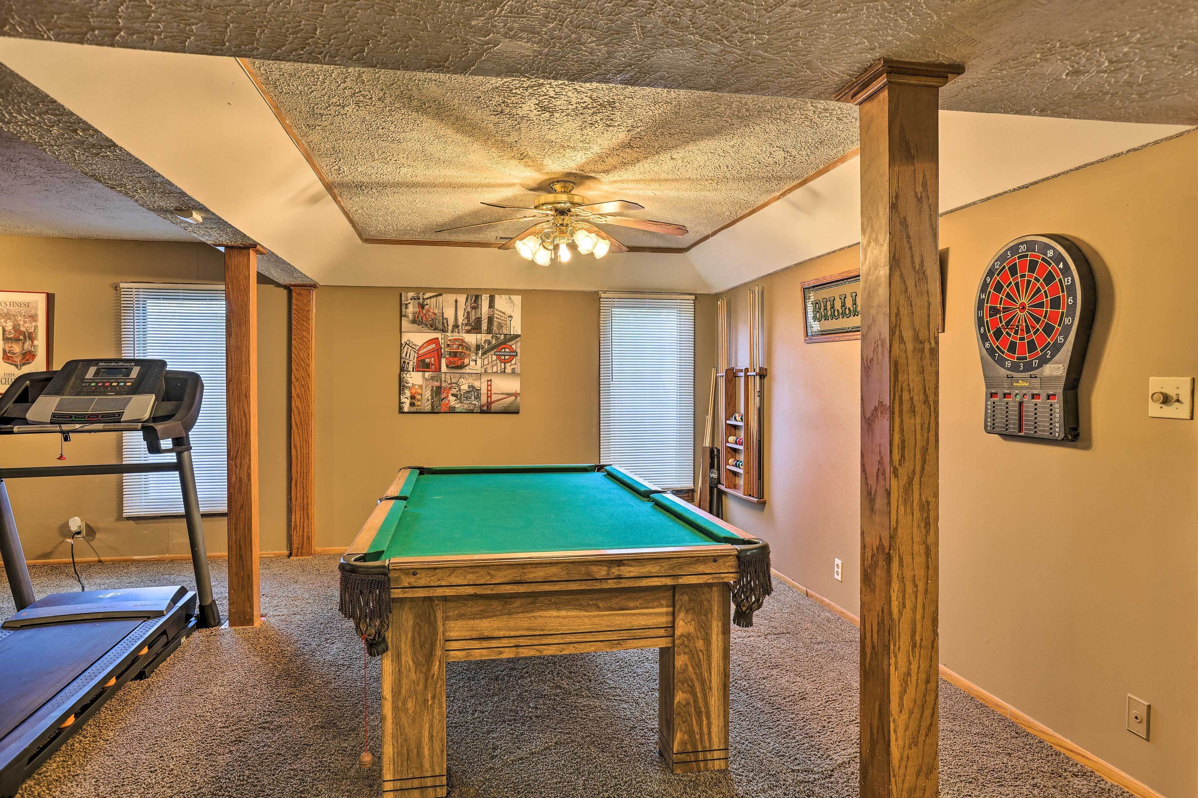 A room with a pool table, a treadmill, and a dartboard.