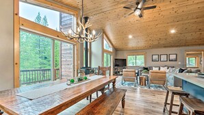 Un vaste espace de vie comprenant une grande table à manger en bois, un ventilateur de plafond et une vue sur l’extérieur.