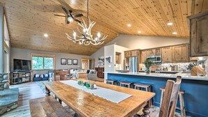 Un vaste espace de vie comprenant une grande table à manger en bois, une cuisine équipée d’appareils modernes et un ventilateur de plafond.