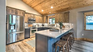 Une cuisine moderne avec des meubles en bois, des appareils en acier inoxydable et un grand îlot central doté de tabourets de bar.