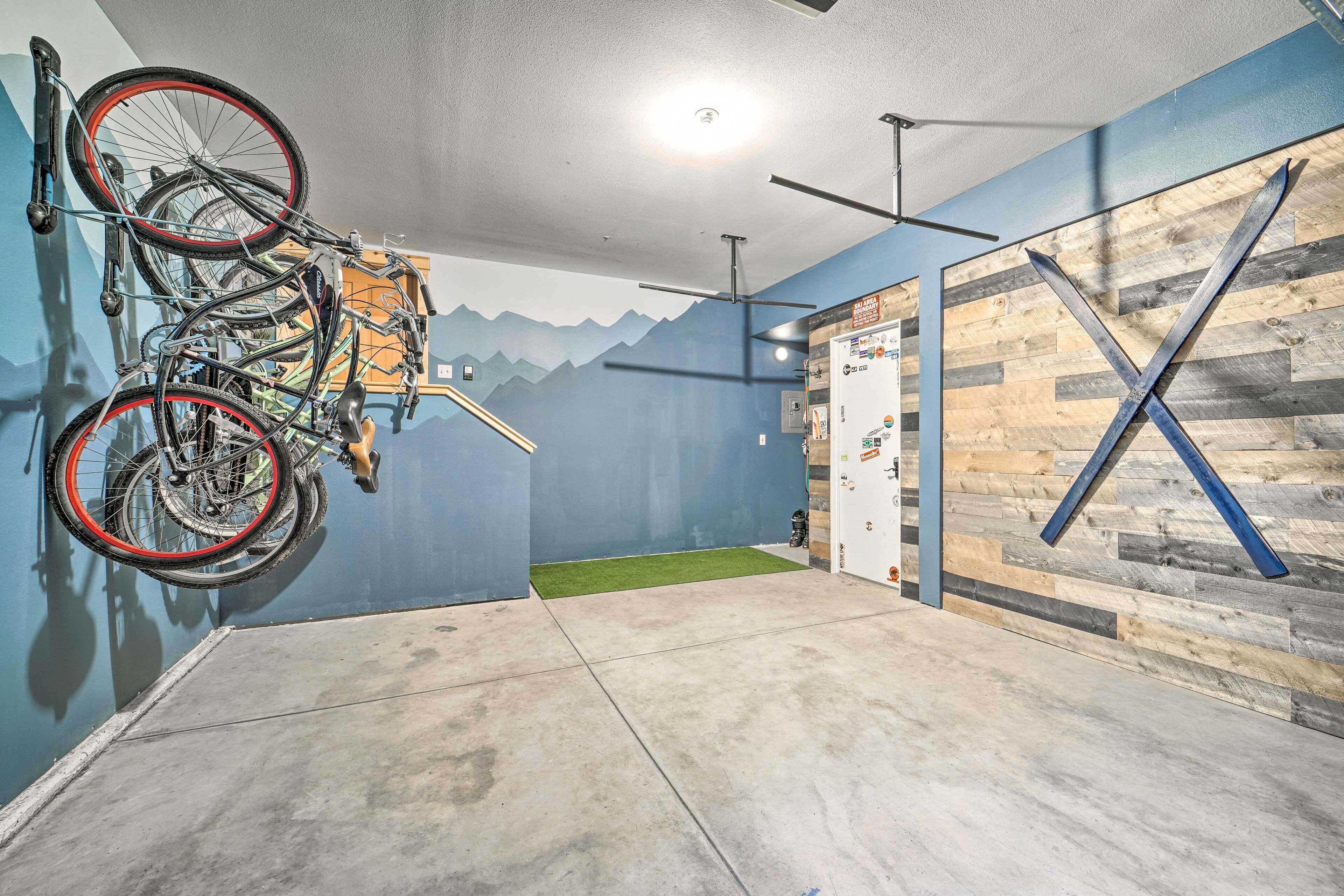 A room with a concrete floor, a ceiling fan, a wall-mounted bike rack, and a wooden wall with a large 'X' decoration.