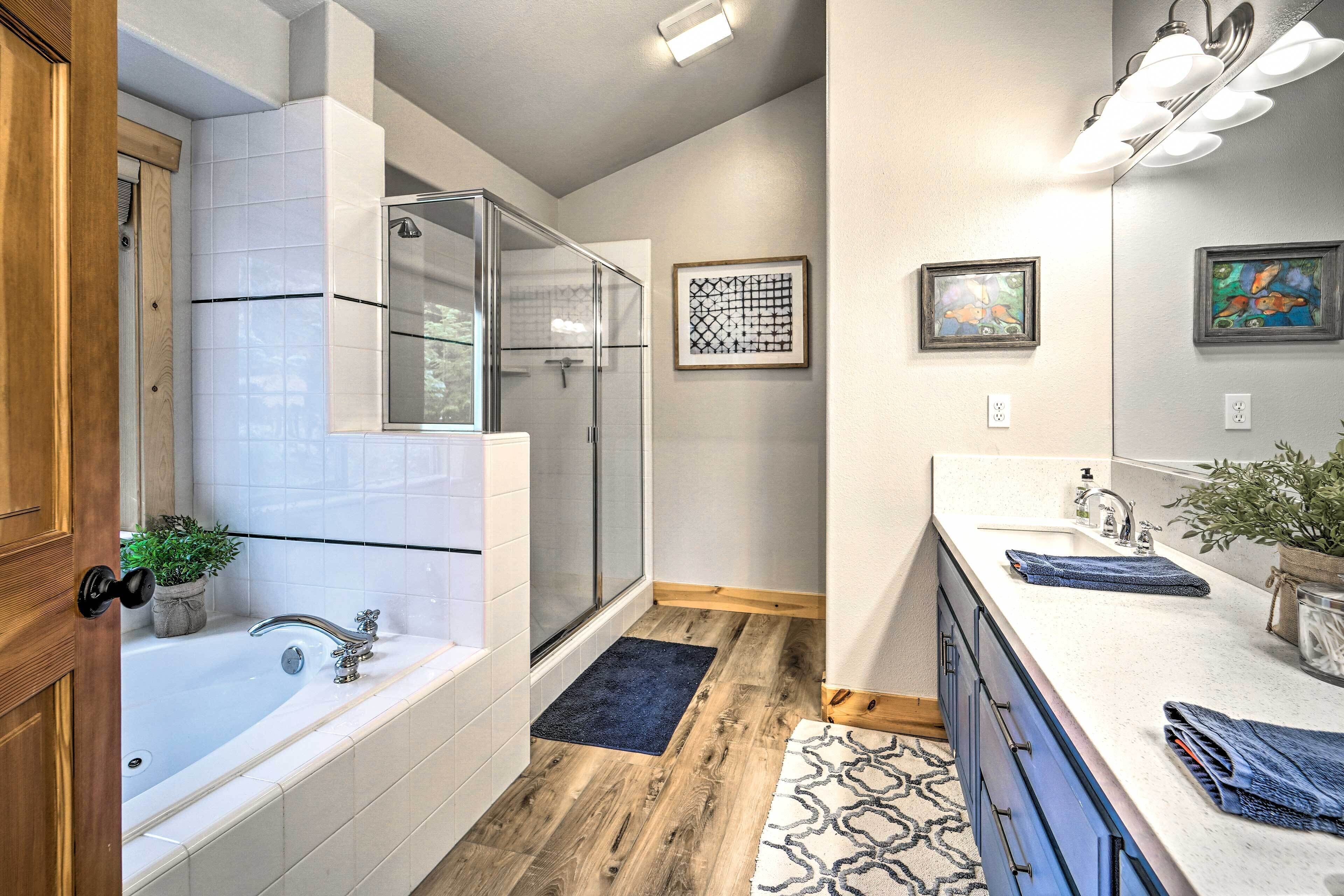 A modern bathroom with a glass-enclosed shower, a bathtub, and a vanity with a sink and mirror.