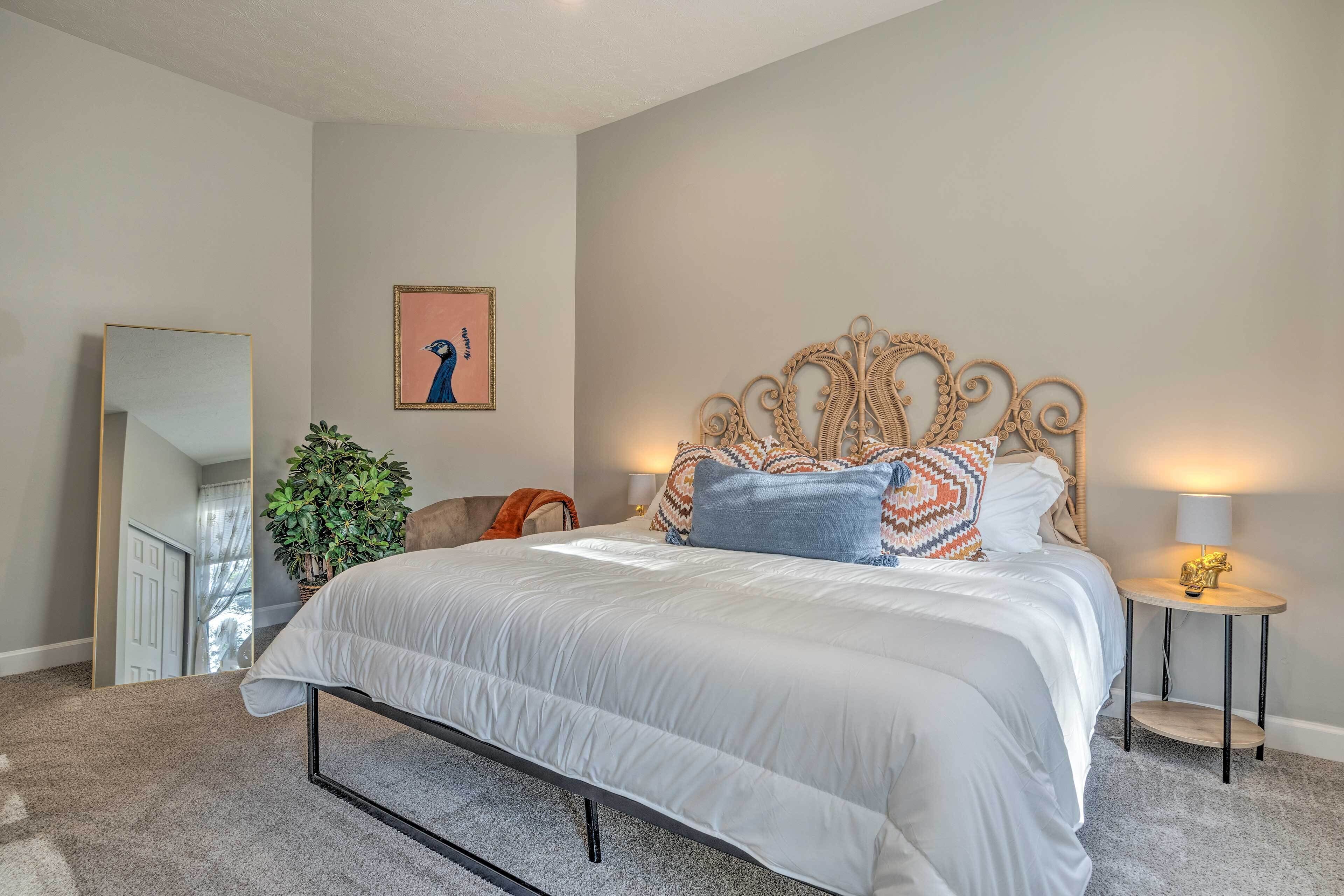 A bedroom with a large bed, a mirror, a plant, and a wall-mounted artwork.