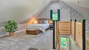 Ein Schlafzimmer mit schrägen Wänden, einem Bett, einem Nachttisch, einer Topfpflanze und einer Holzbank.