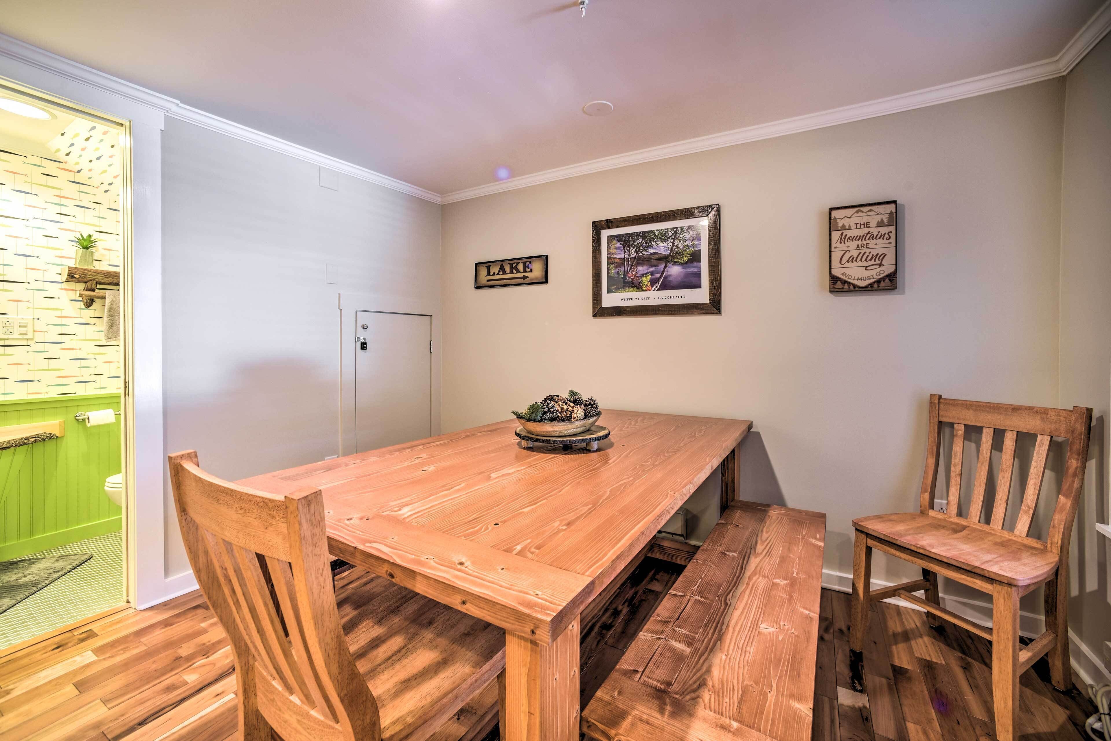 Un coin repas avec une table en bois, deux chaises, un banc et une petite plante posée sur la table.