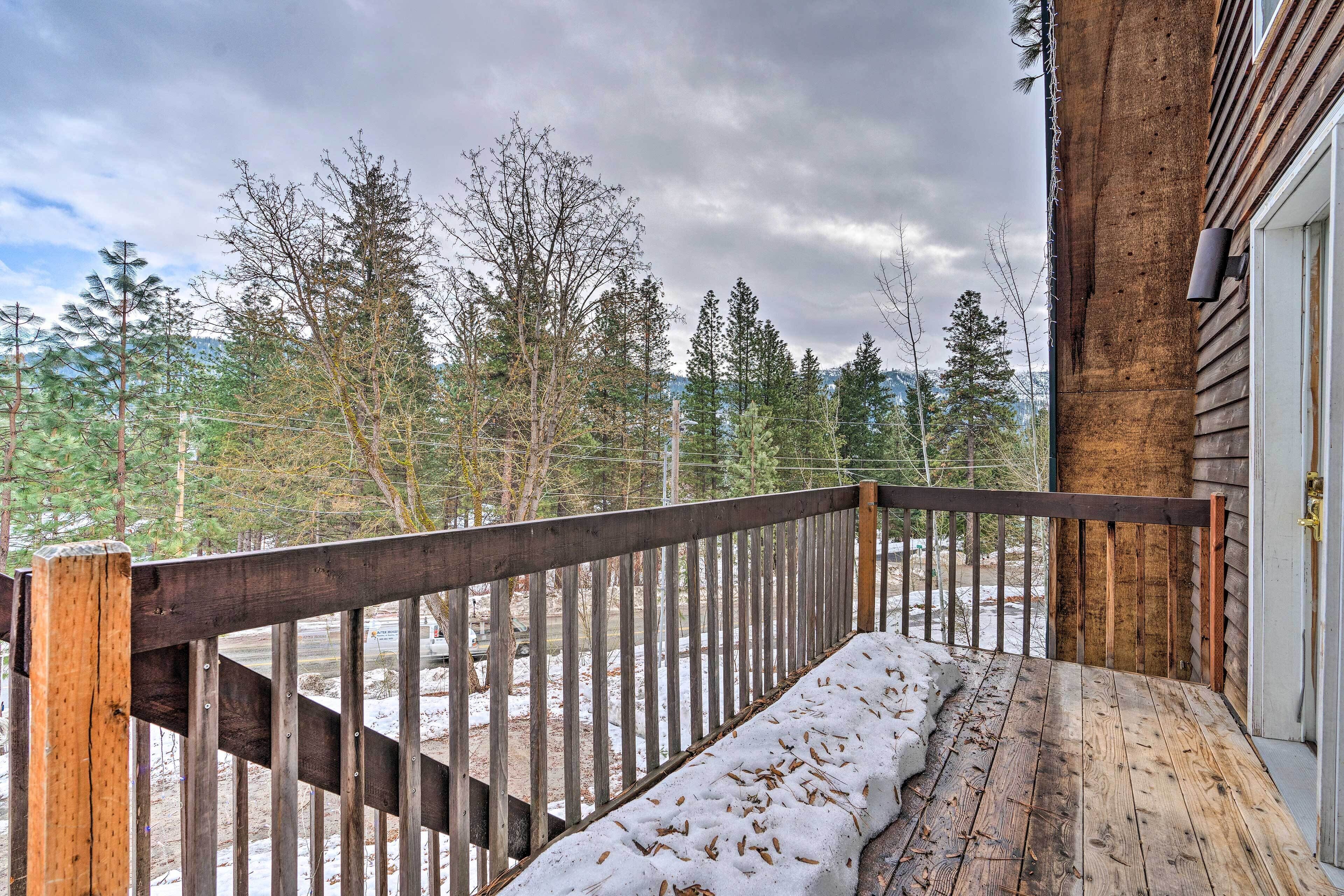 Une terrasse en bois recouverte de neige, une rambarde en bois et, au loin, une vue sur des arbres et des montagnes.