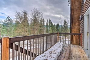 Eine Holzterrasse mit Schnee auf dem Boden, einem Hollergeländer und Blick auf Bäume und Berge im Hintergrund.