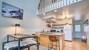 A modern kitchen with a central island, wooden bar stools, a dining table with a white fluffy rug, and a staircase leading to an upper level. - Leavenworth Vacation Rental Near Downtown! (Leavenworth)