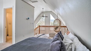 A bedroom with a sloped ceiling, a bed, a hanging chair, and a view of the outdoors. - Leavenworth Vacation Rental Near Downtown! (Leavenworth)