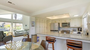 Une cuisine moderne avec des armoires blanches, un comptoir en granit et des appareils électroménagers en acier inoxydable. On y trouve également un coin repas avec une table et des chaises en verre.