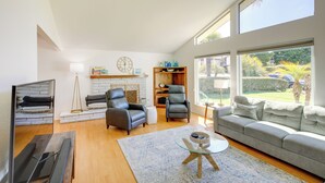 Un vaste salon doté d’une cheminée, de fauteuils en cuir, d’un canapé gris et de grandes fenêtres offrant une vue sur l’extérieur.