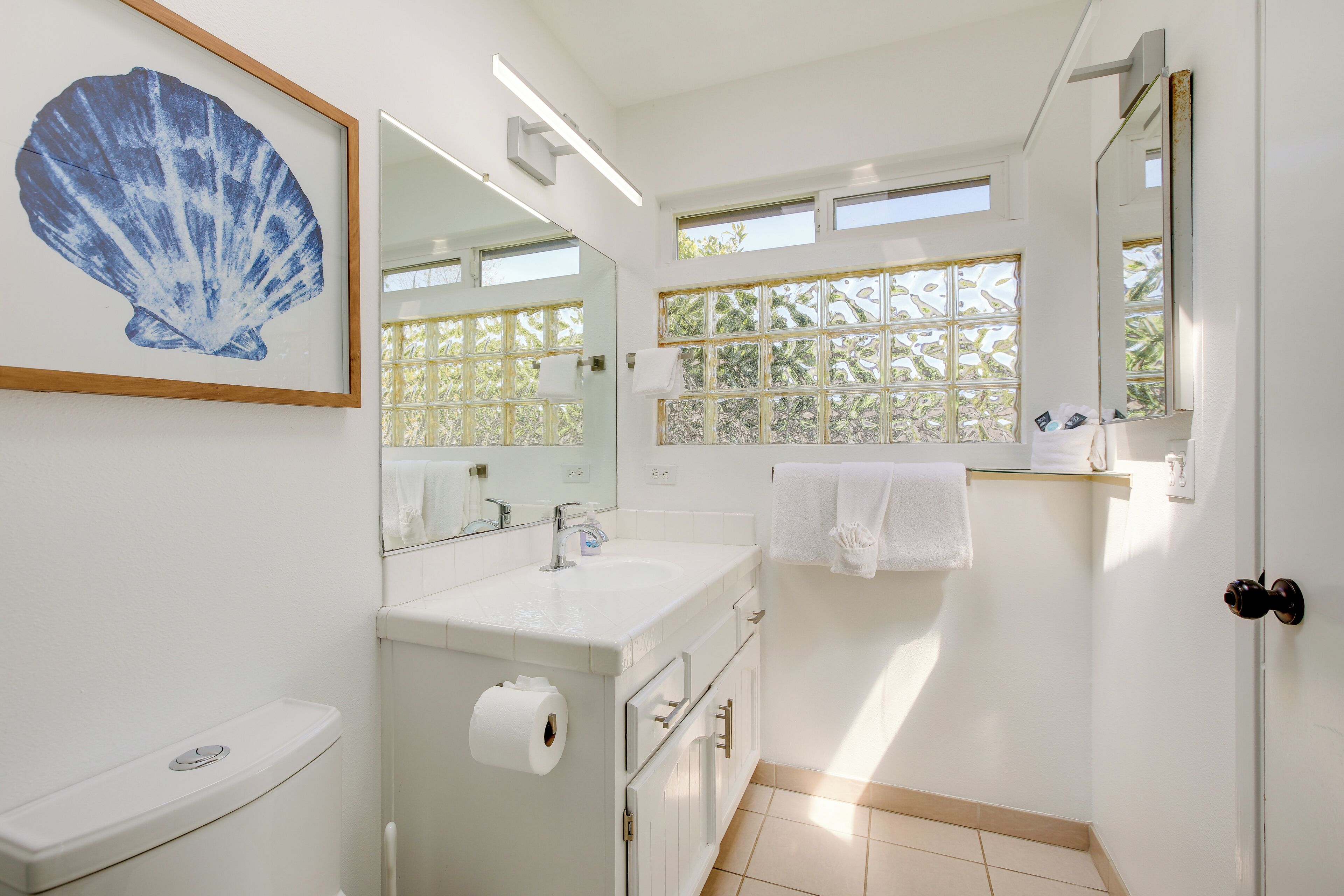A bathroom with a toilet, sink, mirror, and a window with a view of greenery.