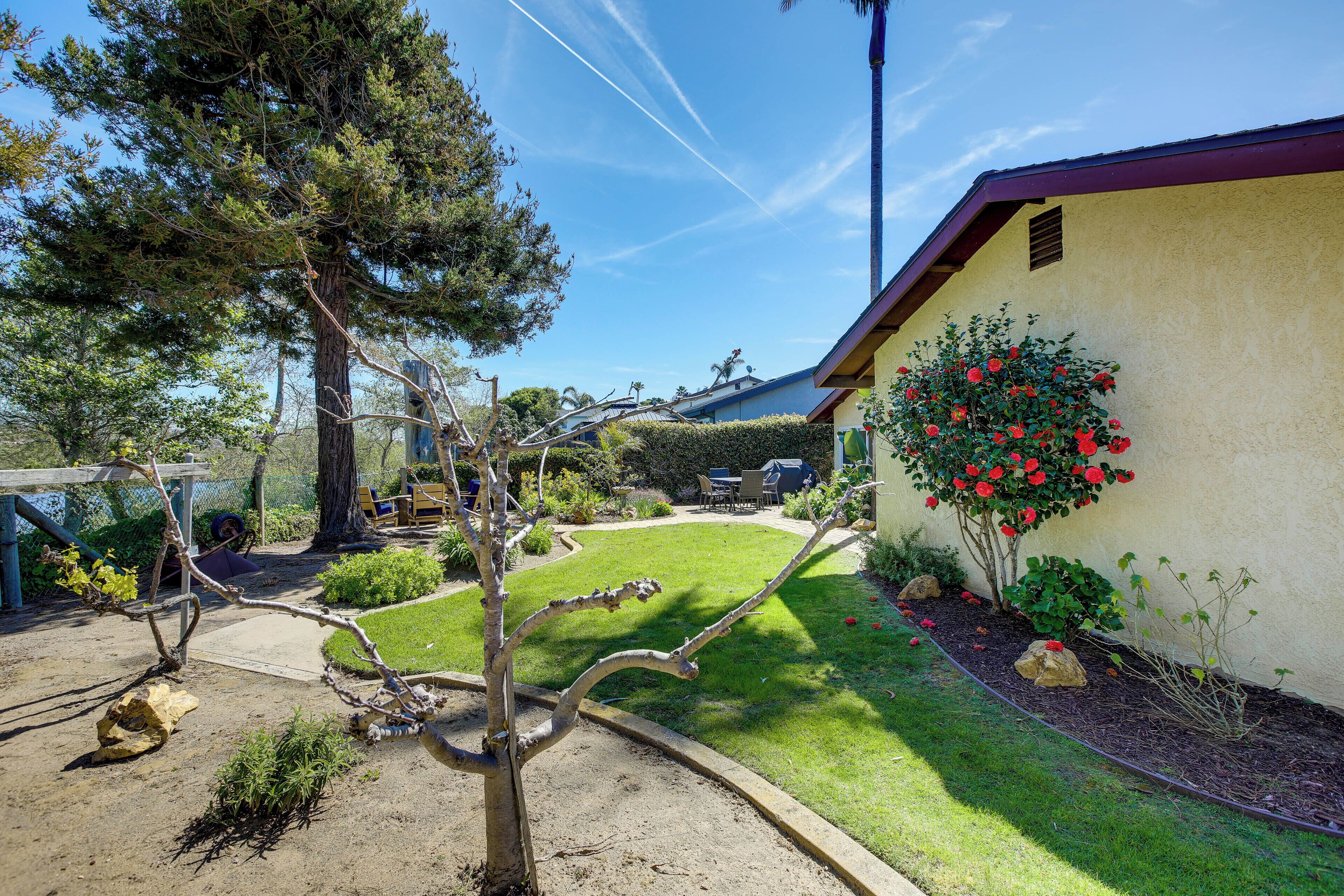 Una propiedad residencial con un césped cuidado, un árbol y un parterre con flores rojas.