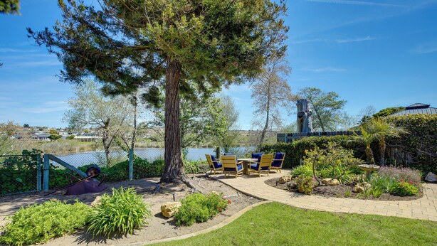 Un espace patio aménagé avec une table et des chaises, entouré de verdure et offrant une vue sur une étendue d’eau.