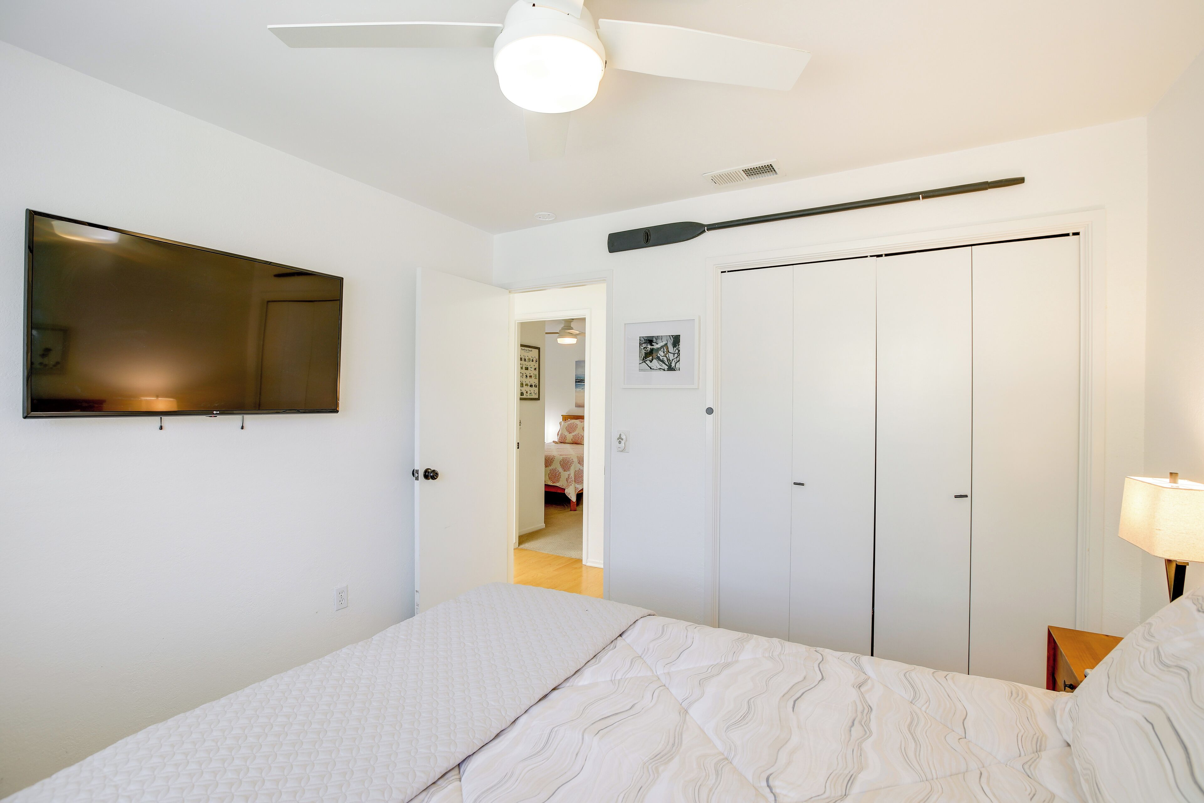 A bedroom with a bed, a ceiling fan, a TV mounted on the wall, and a wardrobe.